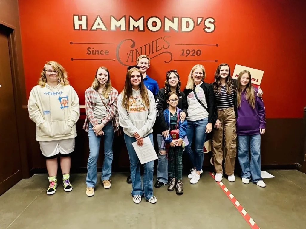 Grupo de ocho personas sonriendo para la cámara delante del cartel "Hammond's Candies Since 1920" en el interior de la tienda.